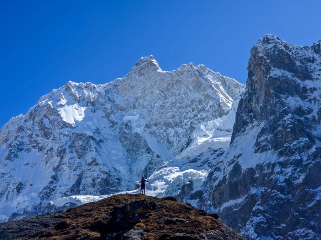 Trekker standing in awe beneath towering snow-covered cliffs on the Kanchenjunga North Base Camp Trek in Nepal