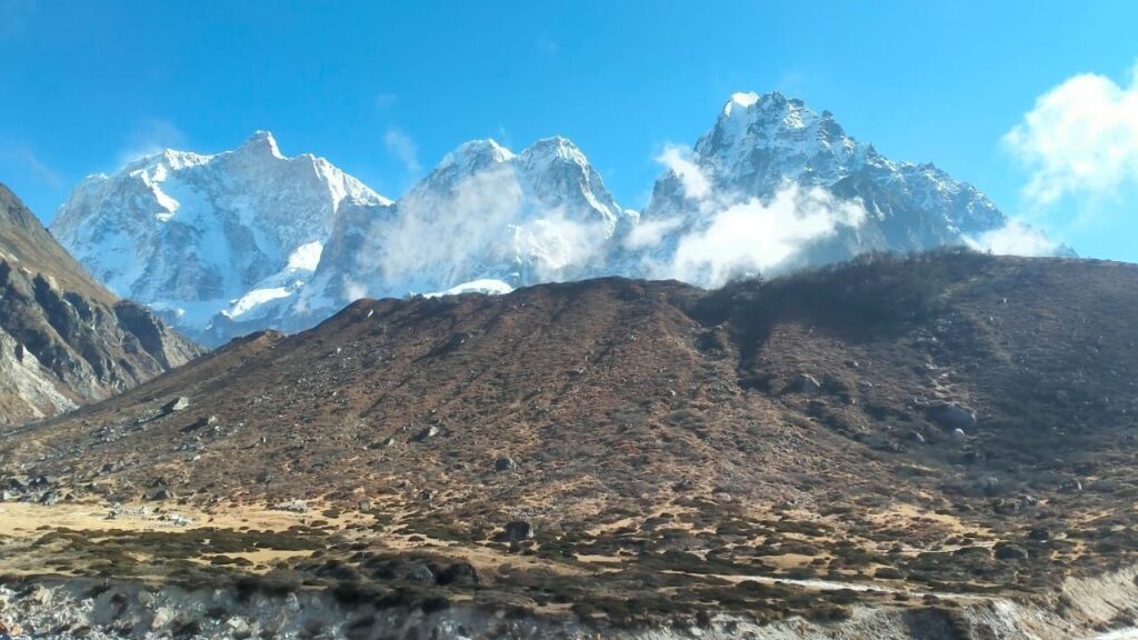 Snow-covered peaks and rugged hills under clear blue skies along the Kanchenjunga North Base Camp Trek in eastern Nepal